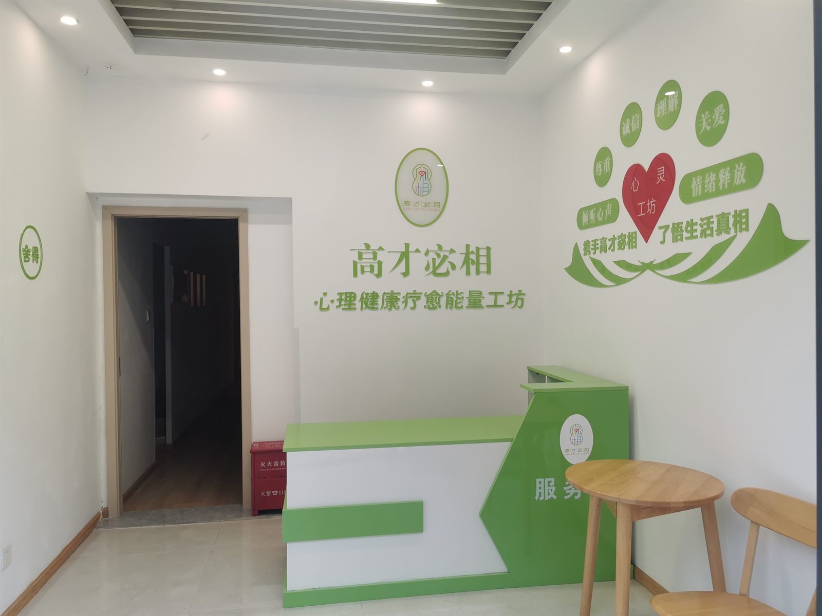 工作室门厅，白墙上为高才宓相标识与「心理健康疗愈能量工坊」字样，右侧是绿色服务台与木质圆桌