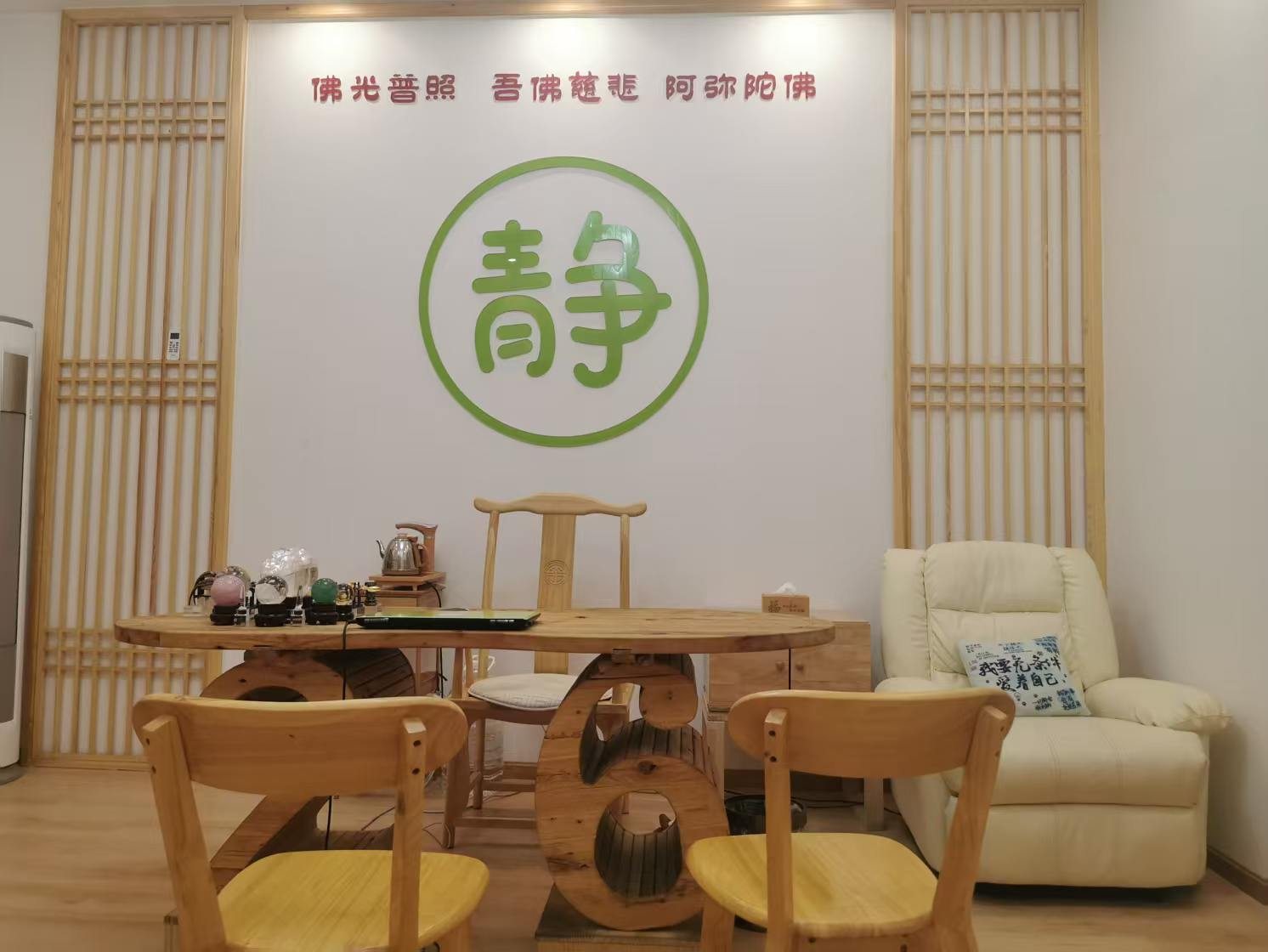 木质格栅之间的白墙上是一面绿色「静」字，前方为原木茶桌与座椅