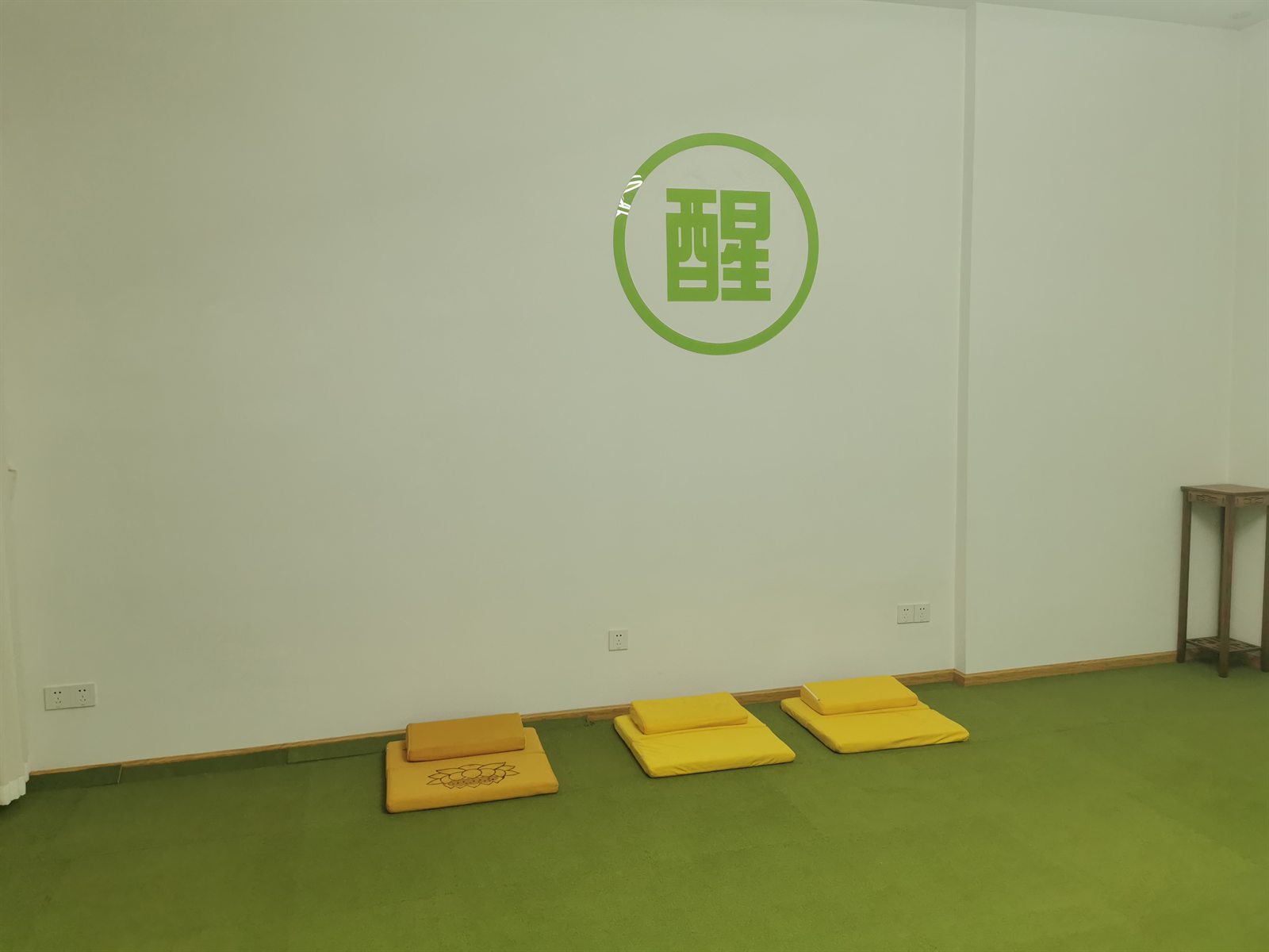 深绿色地毯上摆放着黄色坐垫,墙面为绿色「醒」字标识